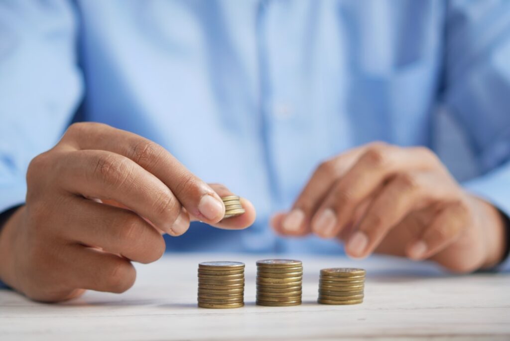 Person carefully stacking coins in rows on a table, representing household budgeting and cost comparisons